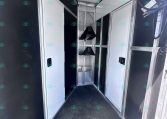 Interior of a dark-colored trailer with white cabinet doors along both walls and a metal center rack for gear; overhead ceiling panels visible.