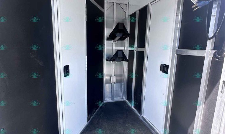 Interior of a dark-colored trailer with white cabinet doors along both walls and a metal center rack for gear; overhead ceiling panels visible.