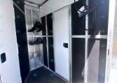 Interior of a metal trailer with silver cabinets, wall hooks, and coiled cables hanging near the ceiling.