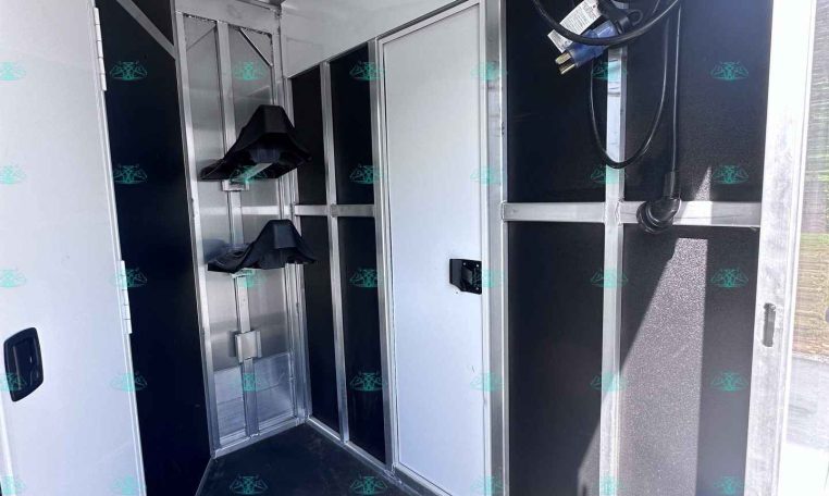 Interior of a metal trailer with silver cabinets, wall hooks, and coiled cables hanging near the ceiling.