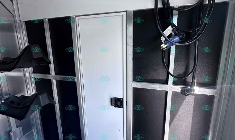 Interior of a metal trailer wall with coiled electrical cords hanging from hooks on the ceiling area