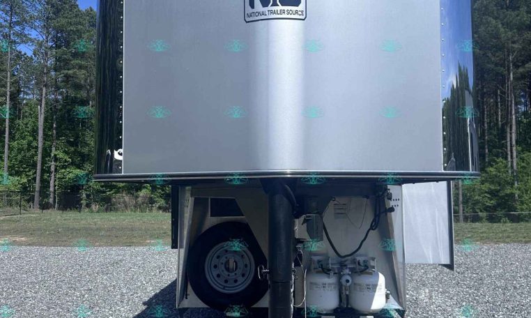 Industrial silver trailer front with NS (National Trailer Source) logo, parked on a gravel lot with trees and blue sky in the background