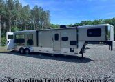 Large white fifth-wheel trailer on a gravel lot with a treeline background and blue sky.