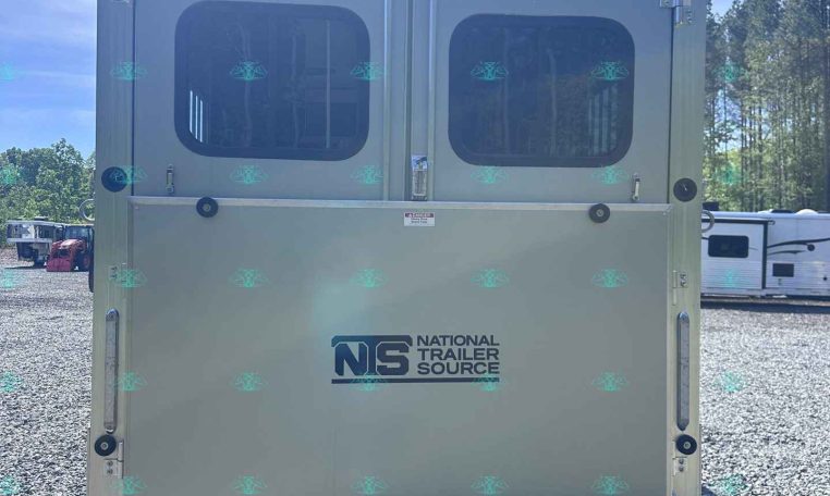Rear of a light-gray trailer with two rear doors featuring rounded windows and the National Trailer Source logo on the lower half, on a gravel lot.