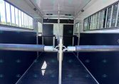 Interior of a horse trailer with a center divider and two side stalls, black lower walls and large side windows.",