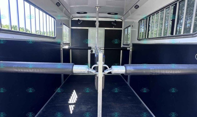 Interior of a horse trailer with a center divider and two side stalls, black lower walls and large side windows.",