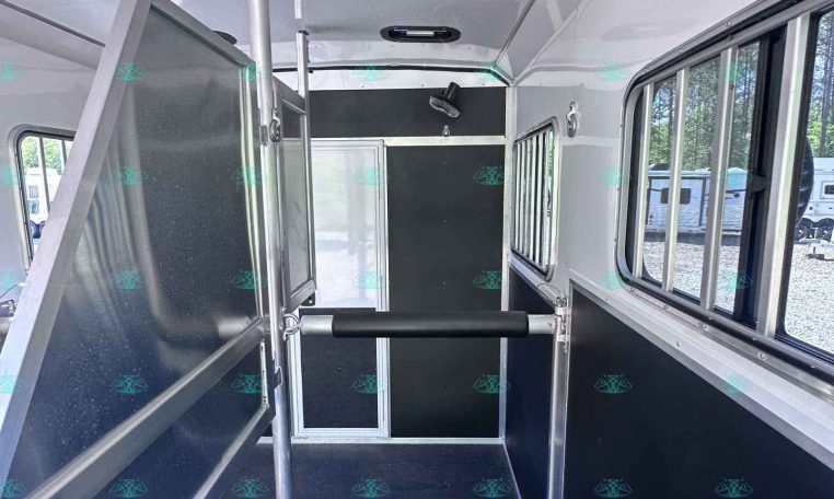 Interior of a horse trailer: central divider, metal framing, and side windows along the stalls
