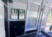 Interior of an aluminum utility trailer showing a small barred window, a ceiling vent/fan, and metal divider rails along the walls.