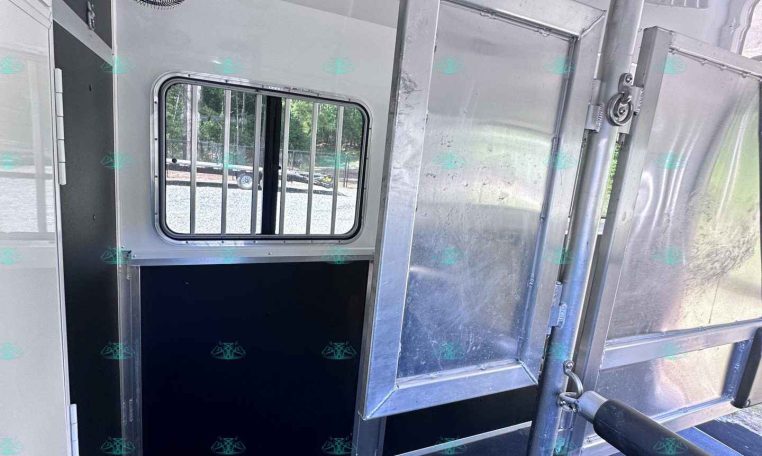 Interior of an aluminum utility trailer showing a small barred window, a ceiling vent/fan, and metal divider rails along the walls.