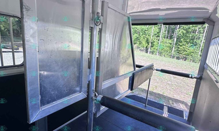 Interior of a metal trailer showing a vertical divider, doorway, and aluminum panels with a black non-slip floor