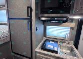 RV kitchen: compact area with a tall black refrigerator, a mounted microwave, and a small sink on a marble-like countertop.