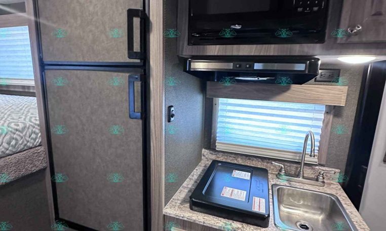 RV kitchen: compact area with a tall black refrigerator, a mounted microwave, and a small sink on a marble-like countertop.