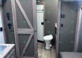 Bathroom inside a travel trailer with a toilet, wood-paneled walls, and gray cabinets including a sliding barn-style door