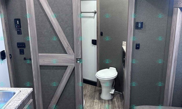 Bathroom inside a travel trailer with a toilet, wood-paneled walls, and gray cabinets including a sliding barn-style door