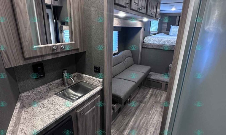 RV kitchen with marble-like countertop, stainless sink, and wood-tone cabinets overheads