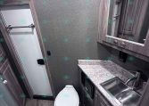 Small bathroom in a trailer with a toilet, sink, and mirrored cabinet above a marble countertop.