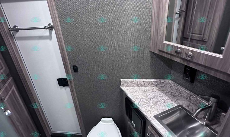 Small bathroom in a trailer with a toilet, sink, and mirrored cabinet above a marble countertop.