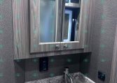 Wood-framed bathroom mirror above a marble countertop with a stainless steel sink and modern faucet, inside a grey-toned RV bathroom.