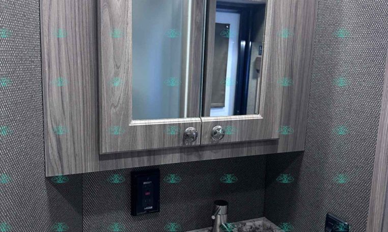Wood-framed bathroom mirror above a marble countertop with a stainless steel sink and modern faucet, inside a grey-toned RV bathroom.