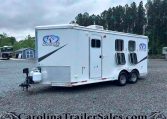 White horse trailer with Charger by Lakota logo parked on gravel lot, trees in background.”] ,
