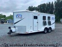 White horse trailer with Charger by Lakota logo parked on gravel lot, trees in background.”] ,