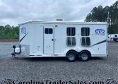 White horse trailer with two axles and barred windows parked on a gravel lot under a cloudy sky, Charger by Lakota logo on the side.