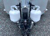 Front view of a trailer hitch with two propane tanks mounted on the tongue and connected hoses.