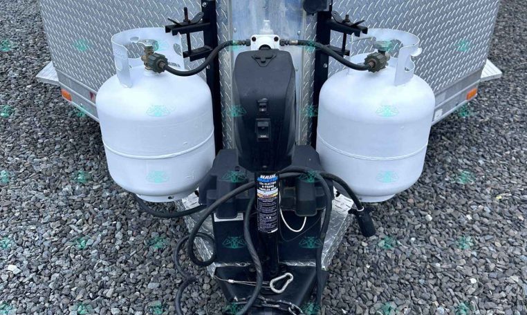 Front view of a trailer hitch with two propane tanks mounted on the tongue and connected hoses.