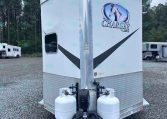 Front view of a white horse trailer with Charger by Lakota logo and a horse head graphic, two propane tanks at the hitch on a gravel lot.