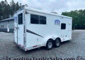 White horse trailer with Charger logo parked on a gravel lot with trees in the background.