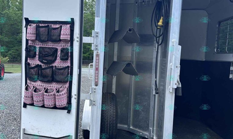 Open aluminum trailer rear with a pink patterned hanging organizer on the door and interior hooks, hoses, and equipment inside.