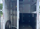 Open horse trailer interior with a center divider, tie rings, and a wheel visible at left, ready for loading.