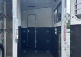 Open horse trailer interior with blue lower walls and metal framing, rear doors swung open.