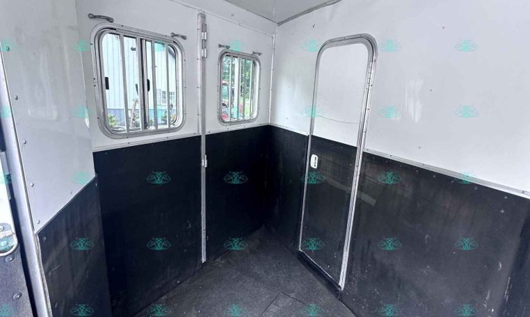 Interior of a small white trailer with two windows and black lower walls, empty stall area.