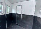 Empty horse trailer interior with white walls, black lower panels, and small side windows