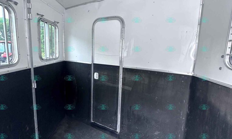 Empty horse trailer interior with white walls, black lower panels, and small side windows
