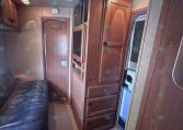 Wood-paneled RV interior with a sofa, built-in cabinets, a microwave, and an entry door visible to the right.