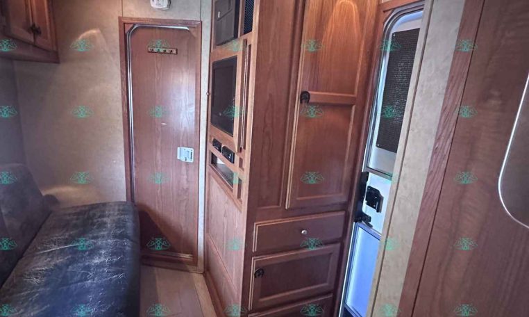 Wood-paneled RV interior with a sofa, built-in cabinets, a microwave, and an entry door visible to the right.