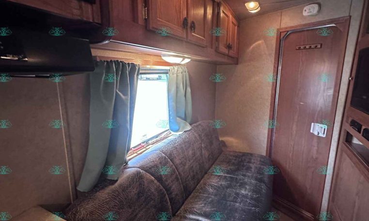 Wood-panelled RV living area with a brown sofa, overhead cabinets, and a window with blue curtains