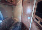 Interior of an RV/trailer living area with wooden cabinets, a brown door, and a dark blue patterned sofa on the left.