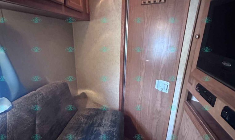 Interior of an RV/trailer living area with wooden cabinets, a brown door, and a dark blue patterned sofa on the left.