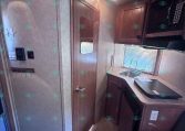 RV kitchen area with dark wood cabinets, sink under a window, and a mounted microwave above the counter.",