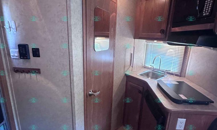 RV kitchen area with dark wood cabinets, sink under a window, and a mounted microwave above the counter.",