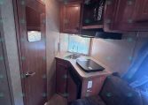 Compact RV kitchen with wooden cabinets, a microwave above the counter, and a sink under a window.