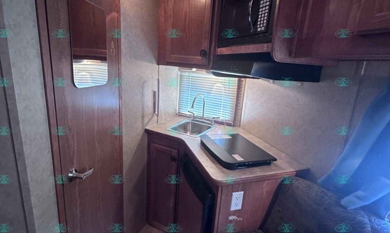 Compact RV kitchen with wooden cabinets, a microwave above the counter, and a sink under a window.