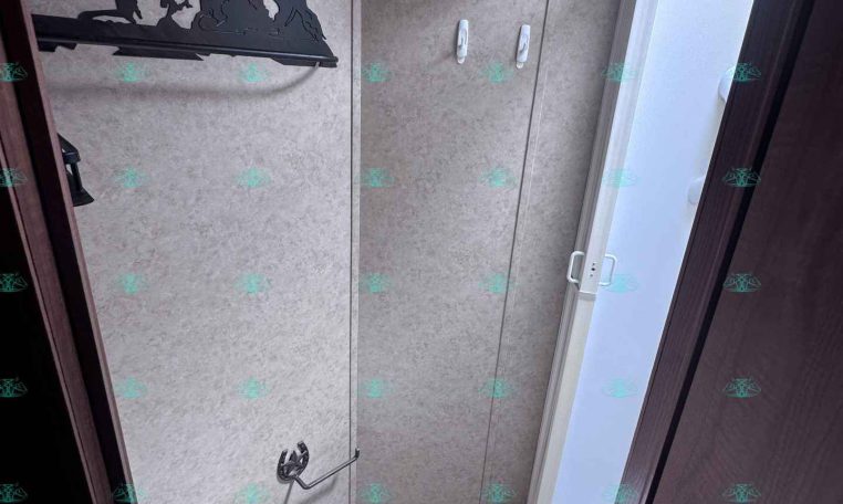 Small RV bathroom with beige panel walls, a white toilet at the floor, and a glass shower door on the right.