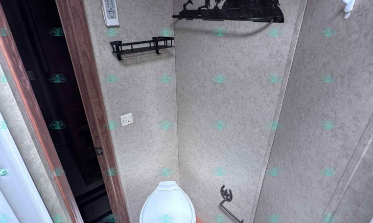 Compact trailer bathroom with beige panel walls, a white toilet, black metal shelves, and a wall mural of galloping horses next to a grab bar.