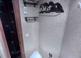 Compact trailer bathroom with a light-blue toilet, two black metal shelves, and a silhouette of horses on the wall.