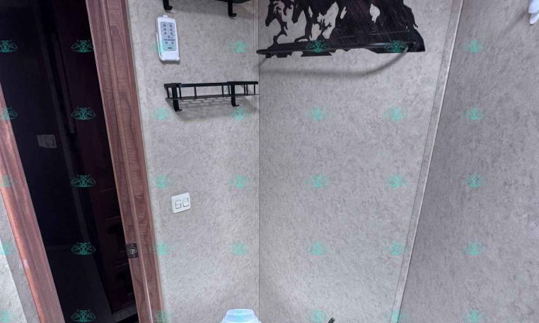 Compact trailer bathroom with a light-blue toilet, two black metal shelves, and a silhouette of horses on the wall.