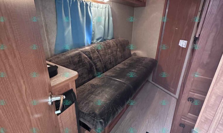 Interior of a small RV living area with brown wood cabinets above a brown upholstered sofa and a light blue curtain along the window